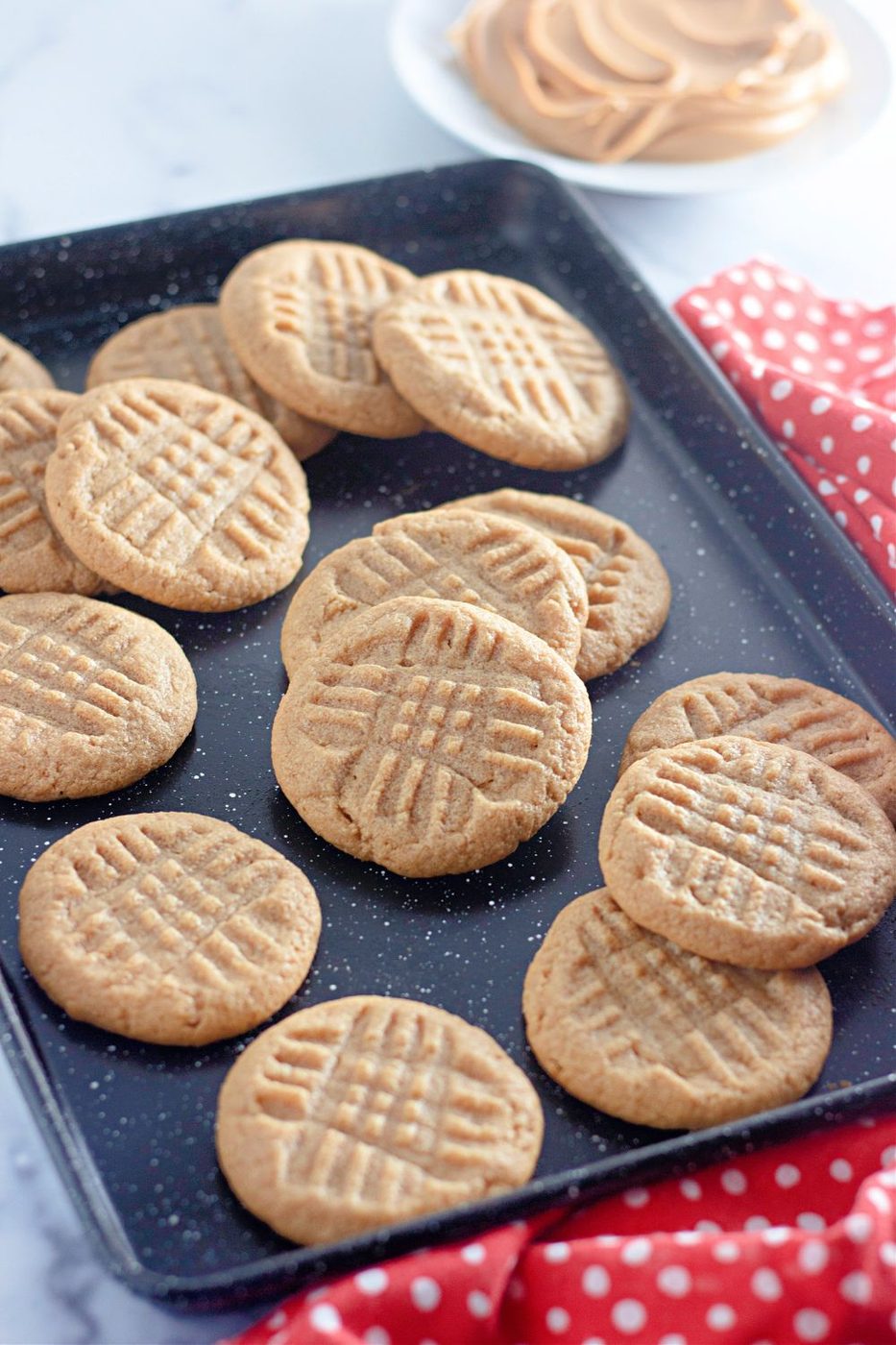 peanut butter cookies on a baking tray stacked on top of each other and scattered on pan