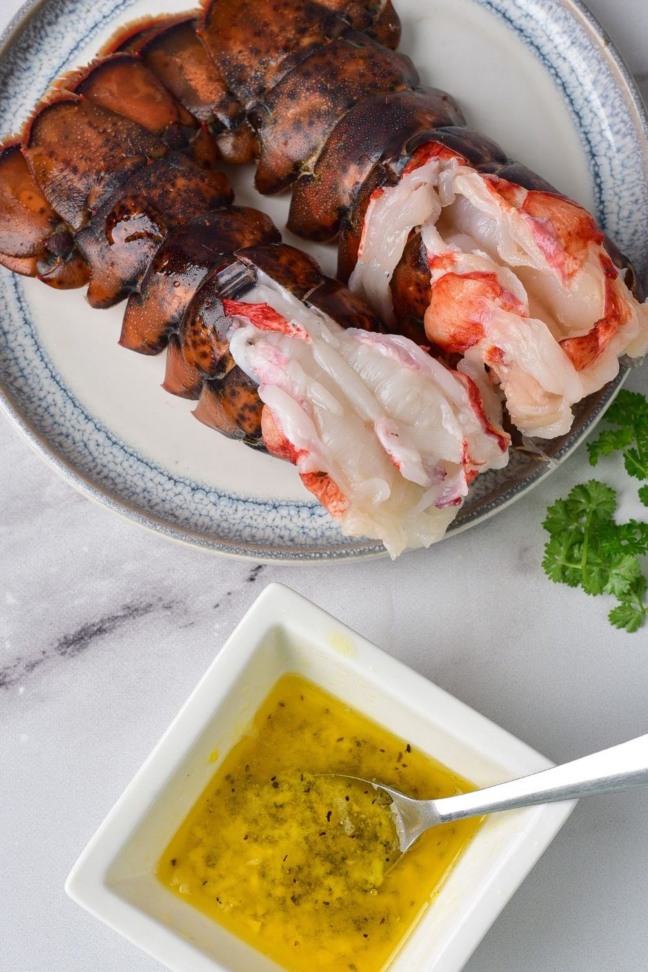 raw lobster tail on plate with garlic butter in a square bowl on table