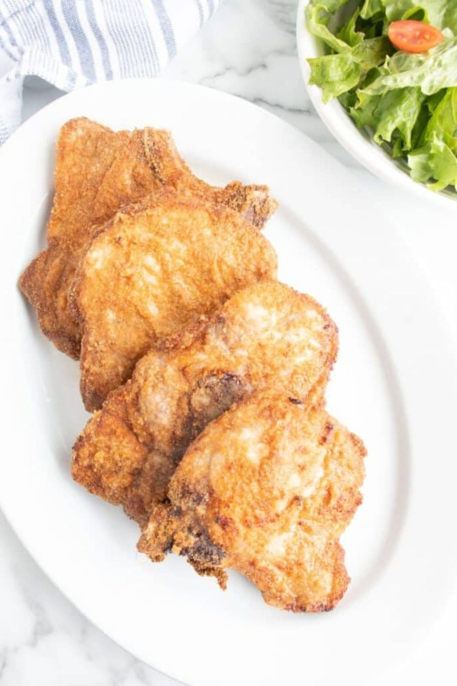 Air Fryer Pork Chops on a serving platter sitting on table with a bowl of salad on the side 