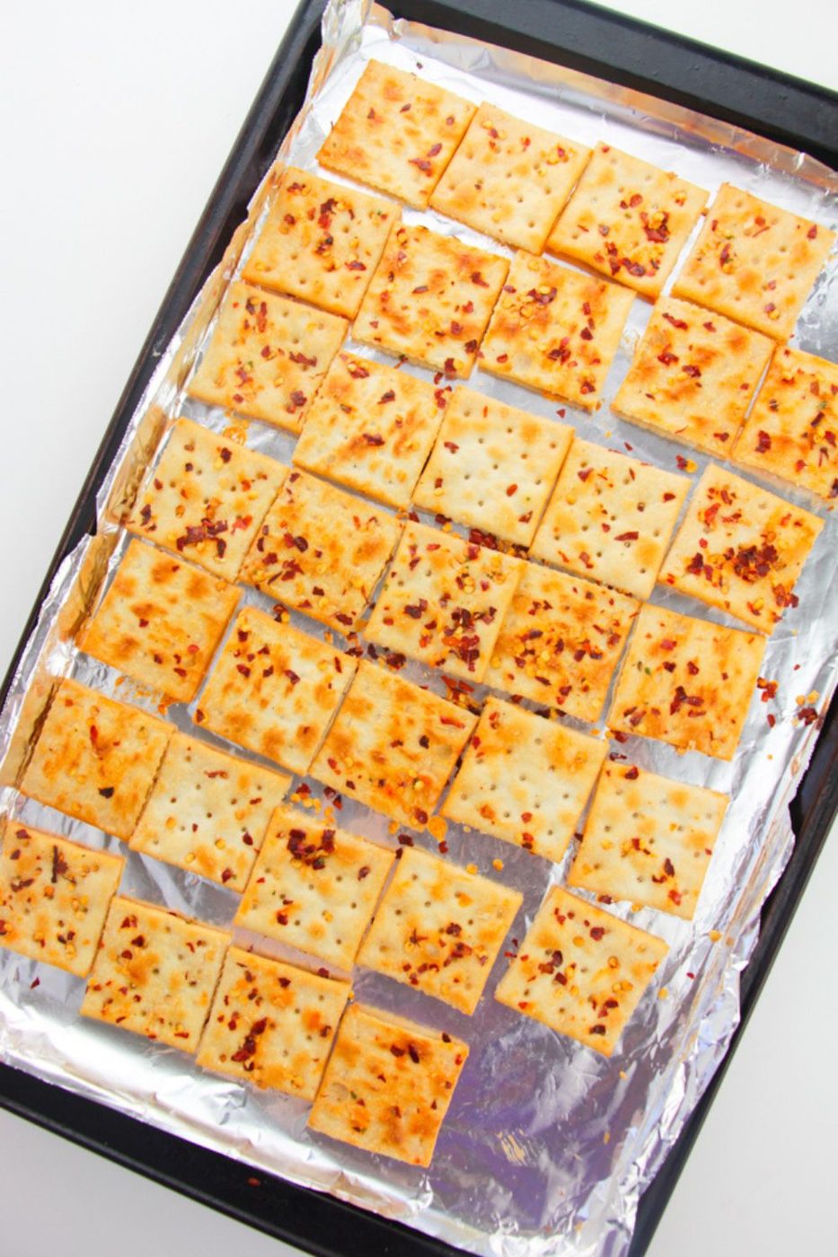 Alabama Heat Crackers spread out on a baking sheet with a foil lined pan 