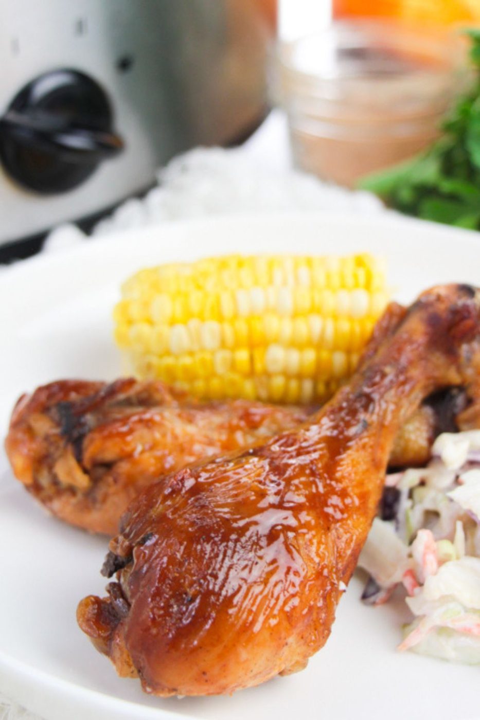 two chicken drumsticks sitting on plate with corn and coleslaw on it 