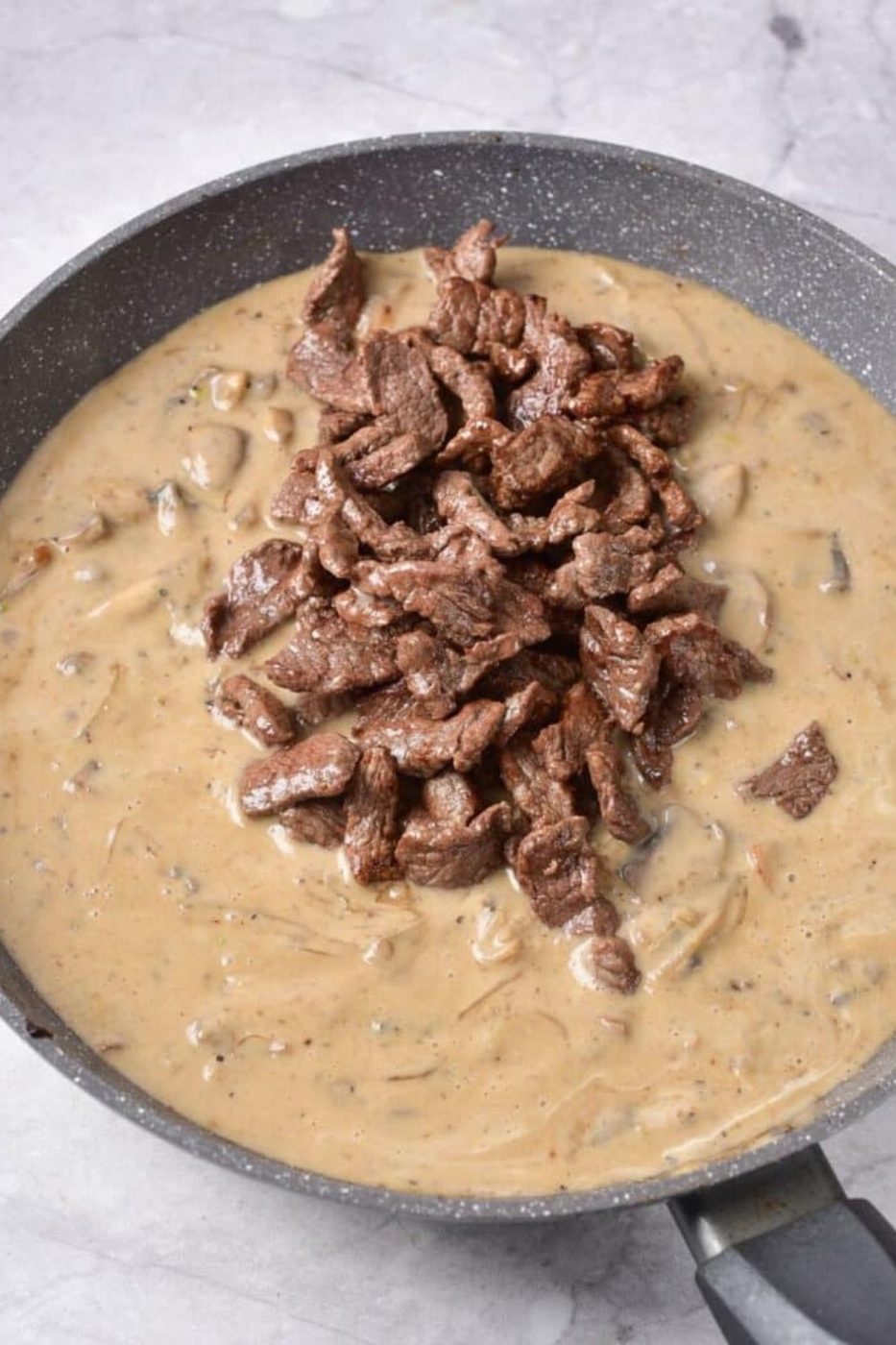 creamy sauce in pan that has a bunch of cooked steak on top 