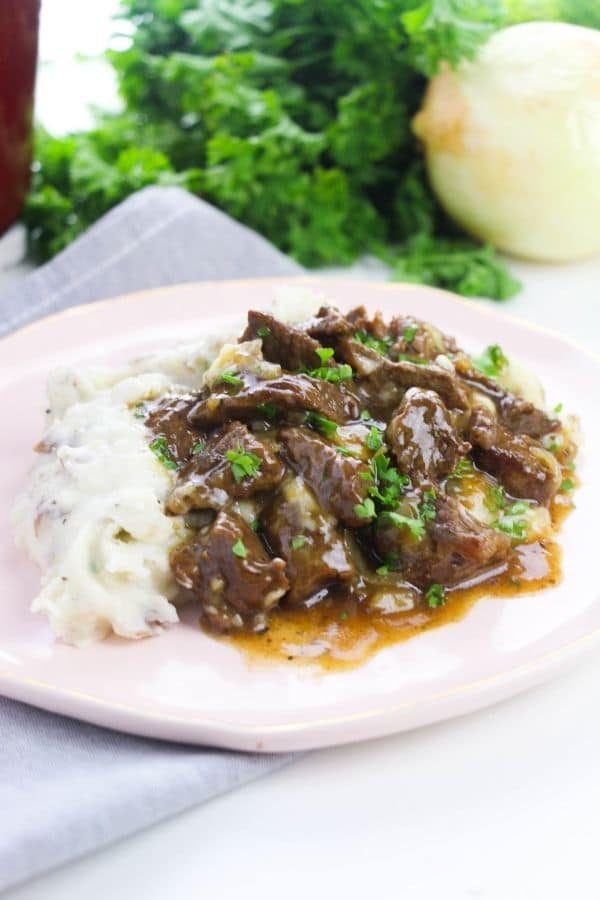 plate of beef and potatoes with onion and garnish behind it