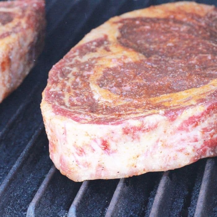 raw steaks on a pellet grill with a dry rub seasoning on top 