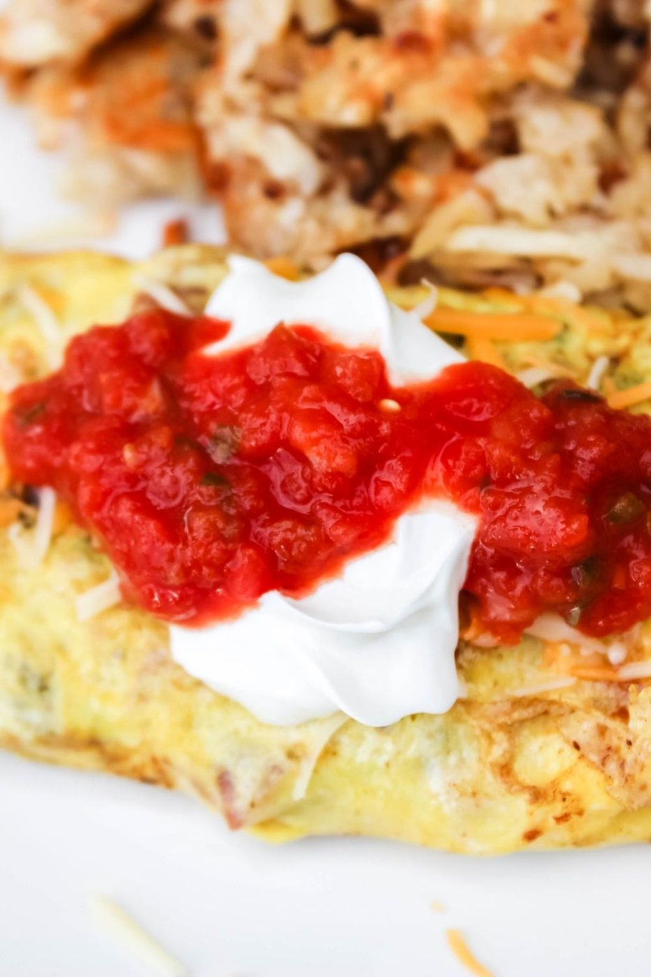 side view of omelette on plate with sour cream and salsa with potatoes on side on white plate 