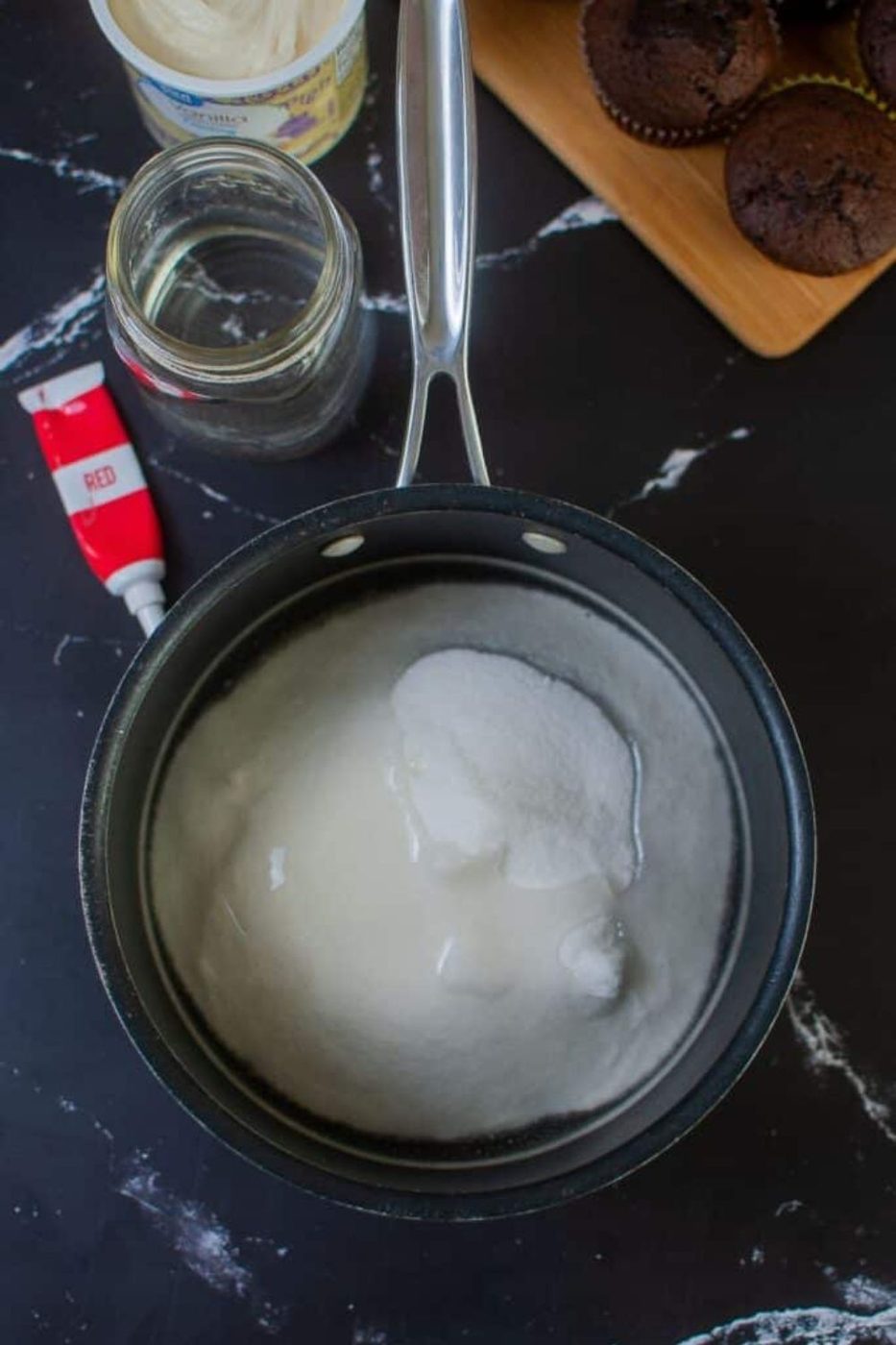 sugar and water in a saucepan on table with food coloring to the side 
