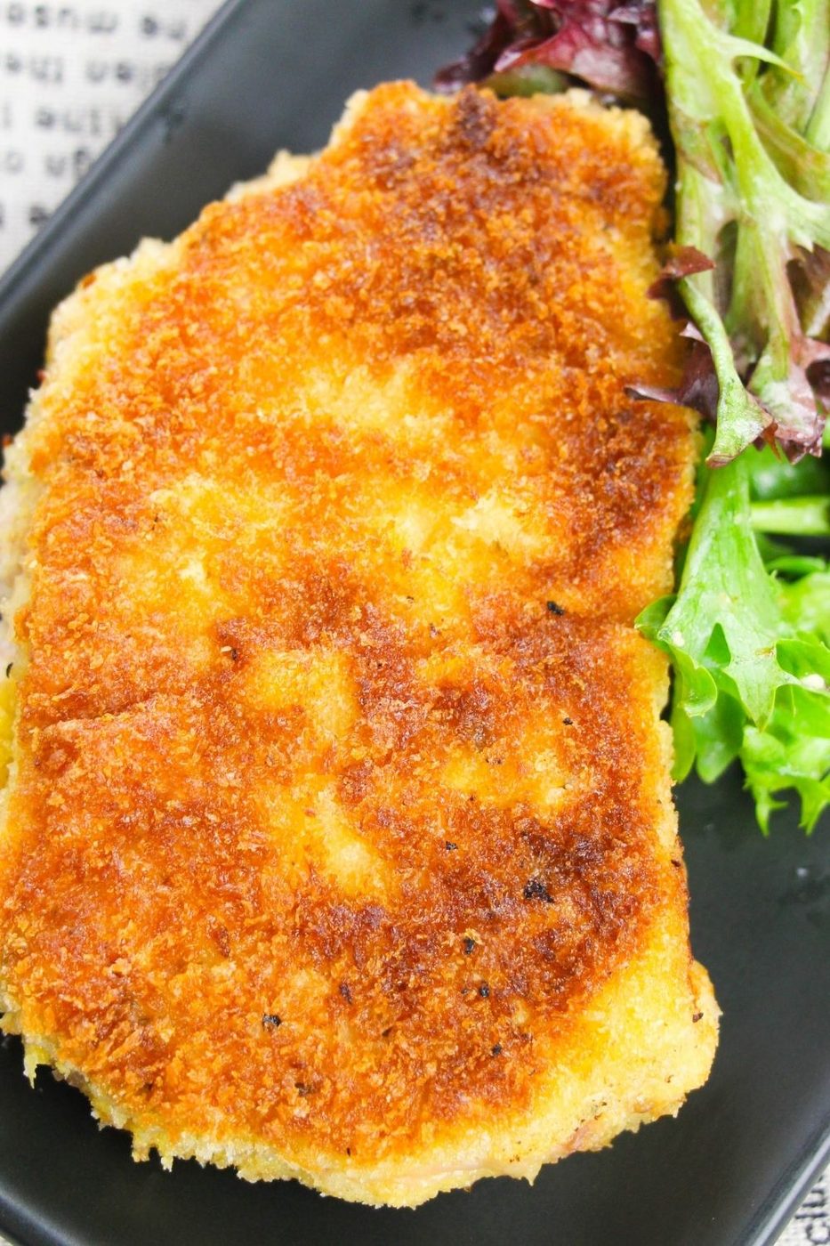 crispy breaded pork chop on black plate with a green salad by it