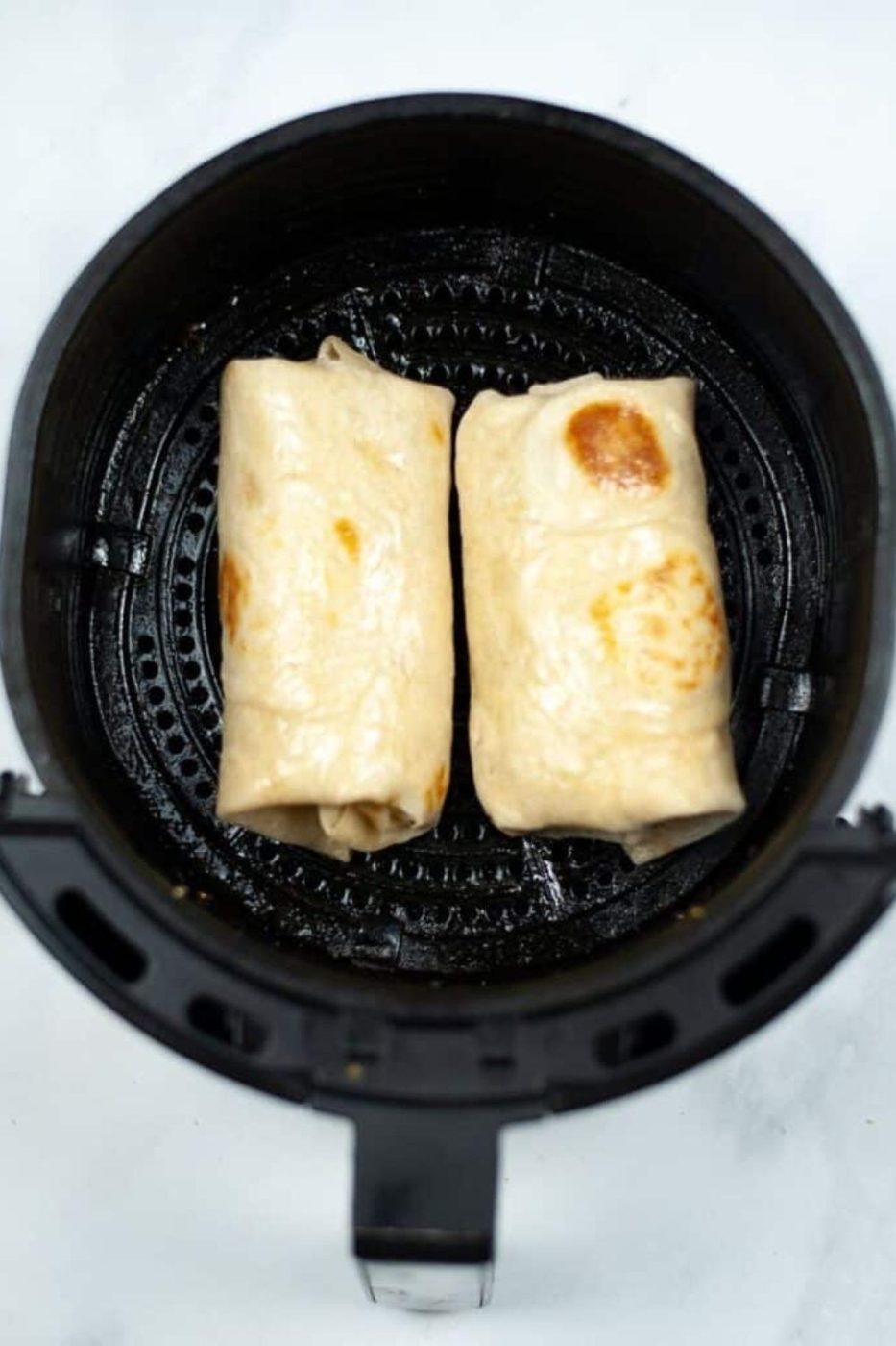 Breakfast Chimichangas in an air fryer basket sprayed with oil 