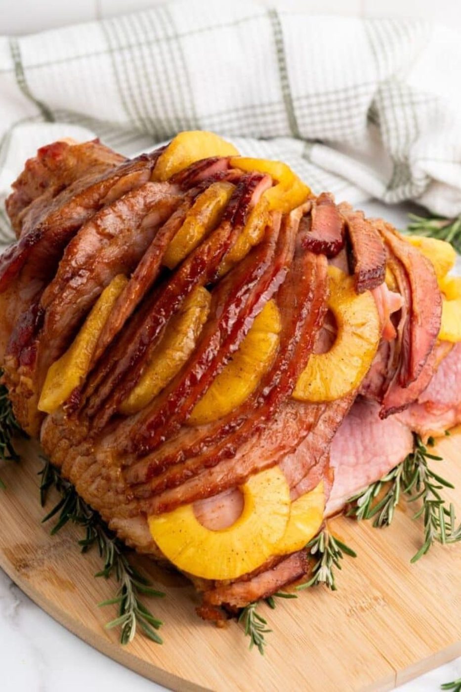 Brown sugar glazed spiral ham with pineapple rings on wooden board