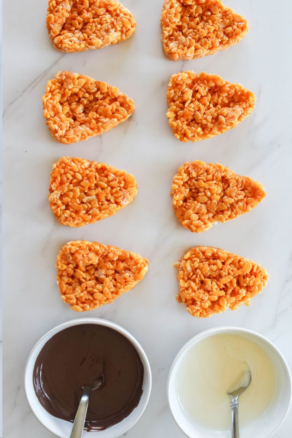 triangle rice crispy treats on table with two bowls of chocolate melted on side