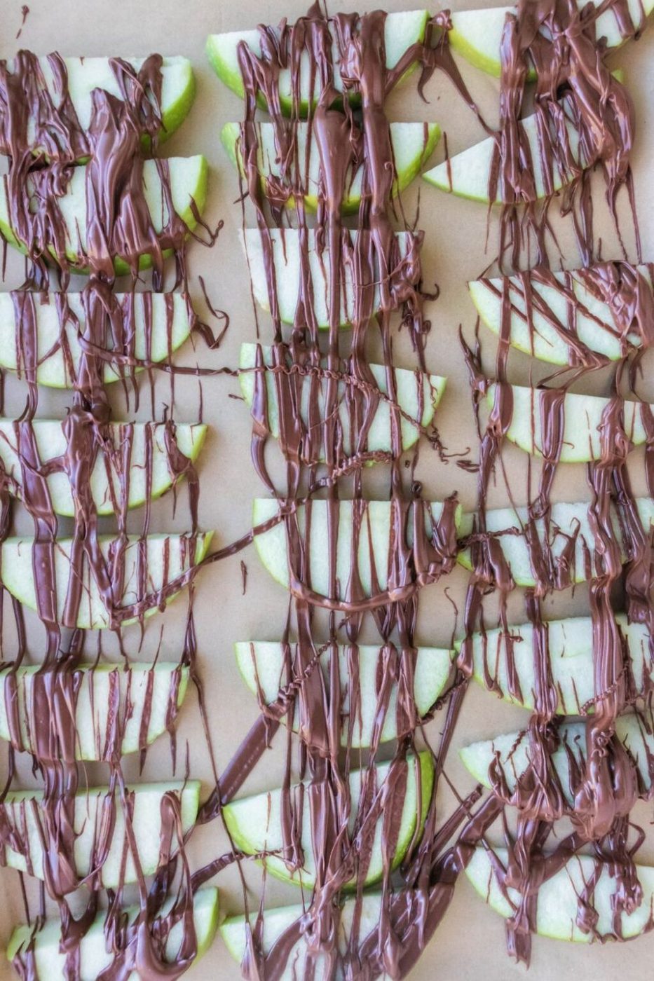 sliced apples on parchment paper drizzled with melted chocolate