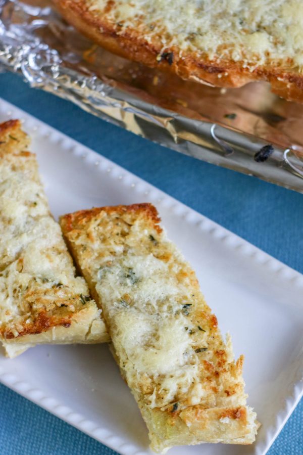 cheesy mozzarella bread on tray and pan of bread behind it