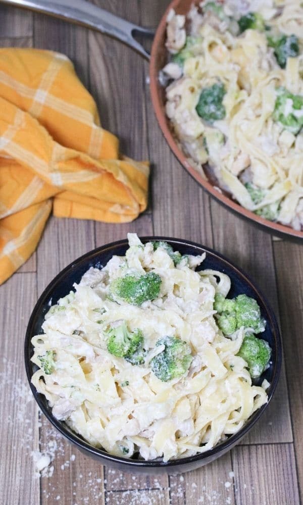 alfredo wth chicken and broccoli in bowl with pan and towel behind it 