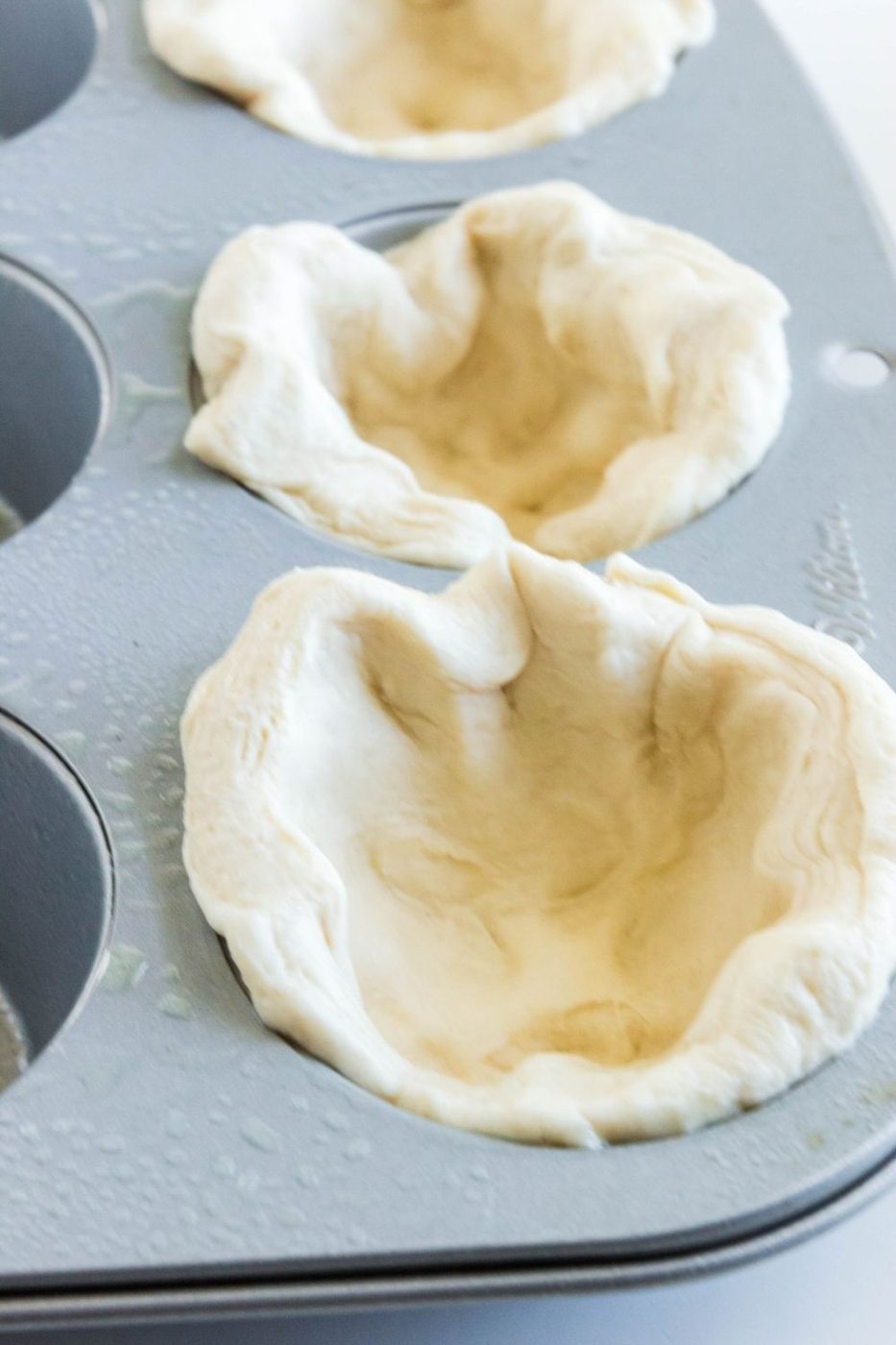 biscuit dough spread out in a muffin tin