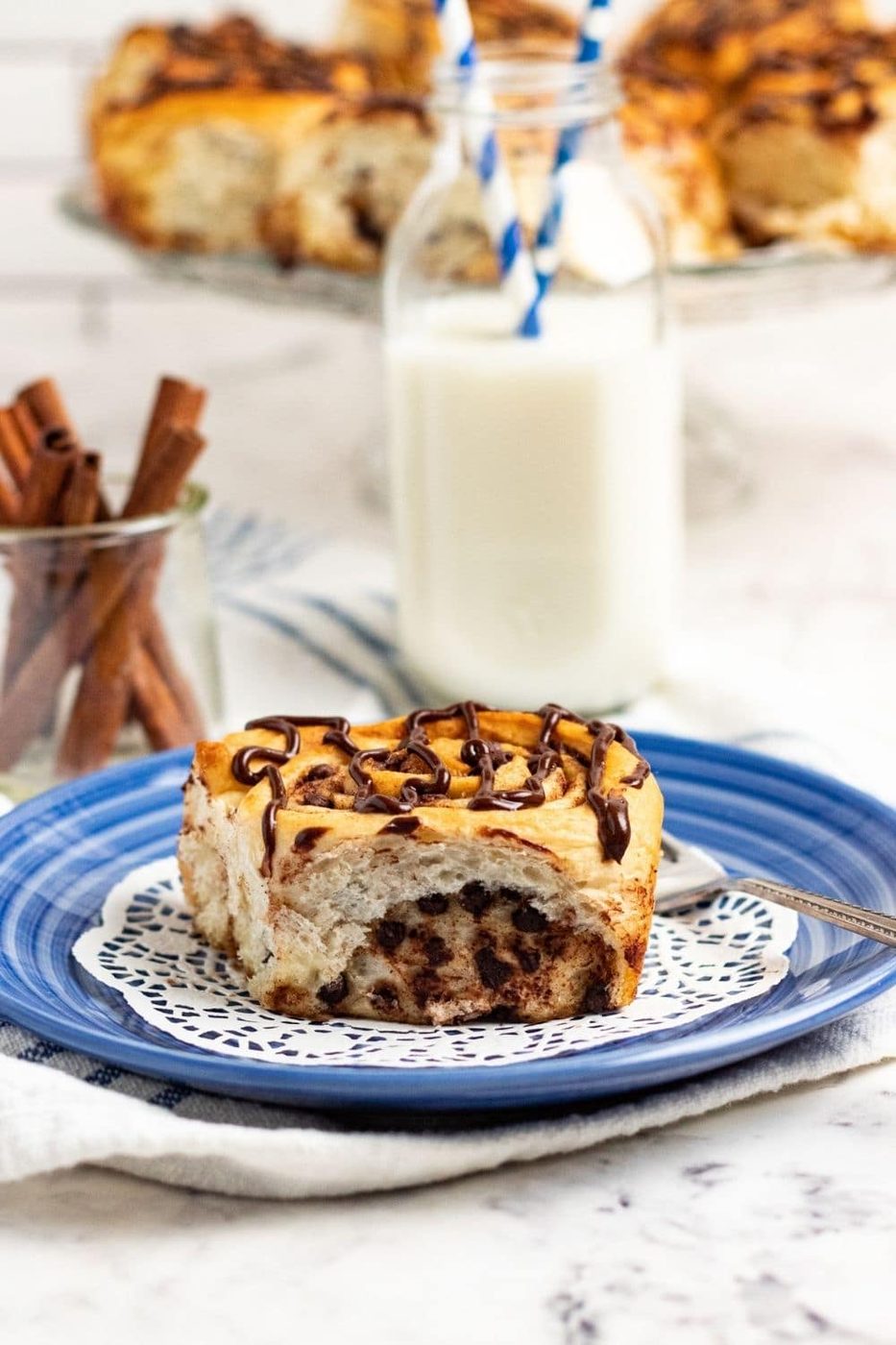 chocolate drizzled cinnamon roll on plate with milk behind it