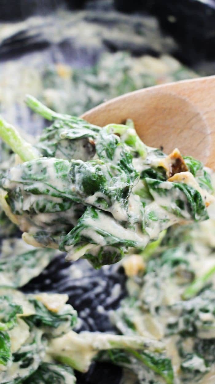 creamed spinach in a skillet with a with wooden spoon scooping some out of the pan