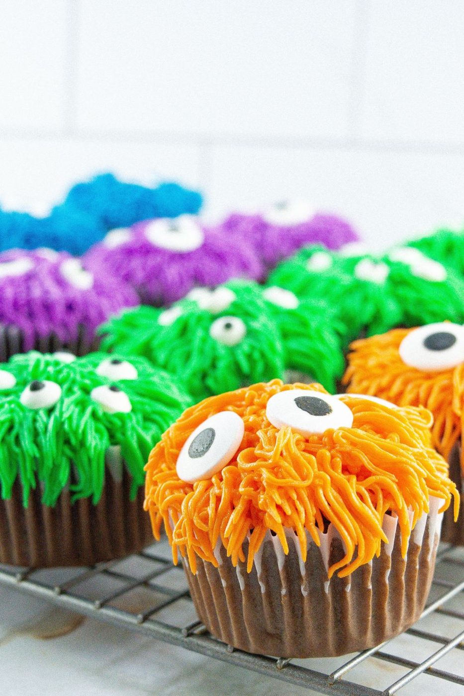 monster decorated cupcakes on a cooling rack on table 
