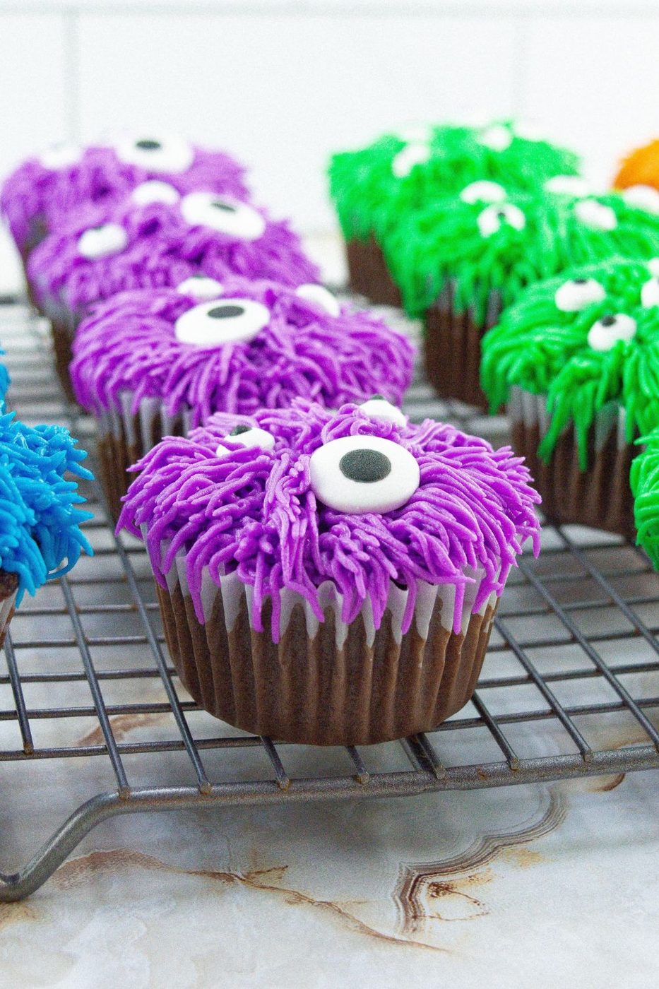 cooling rack with monster designed cupcakes on top 