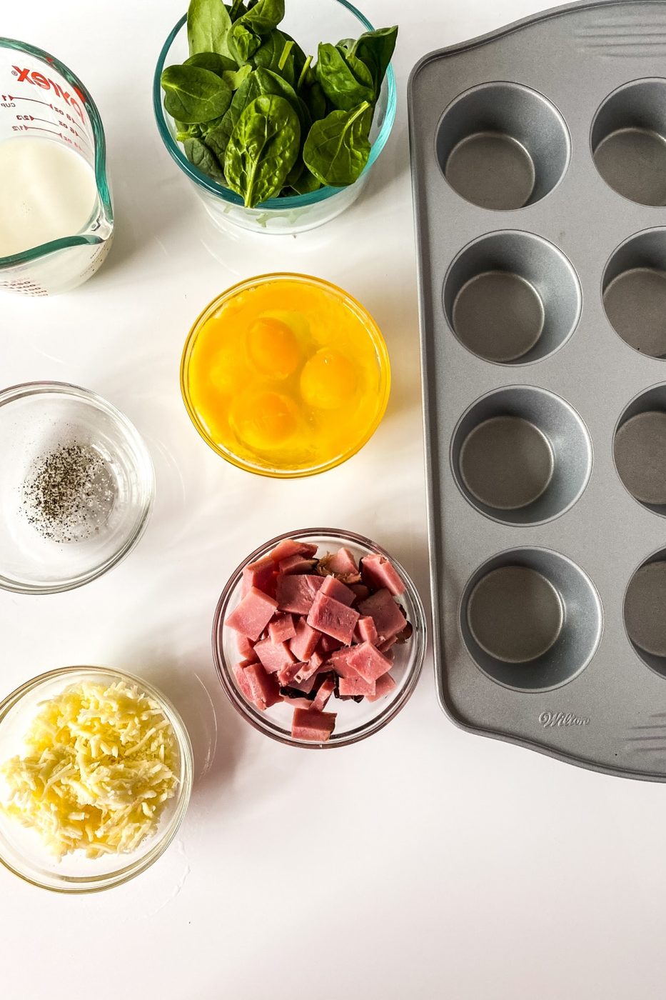 ingredients for egg spinach frittatas on counter with muffin tin by it 