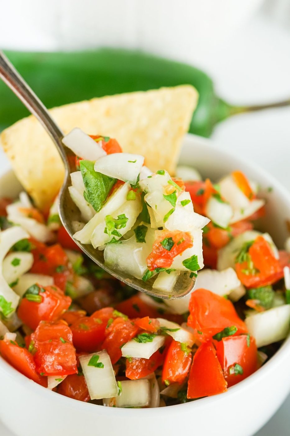 pico de gallo in a white bowl with a spoon of mixture on it to show the vegetables 