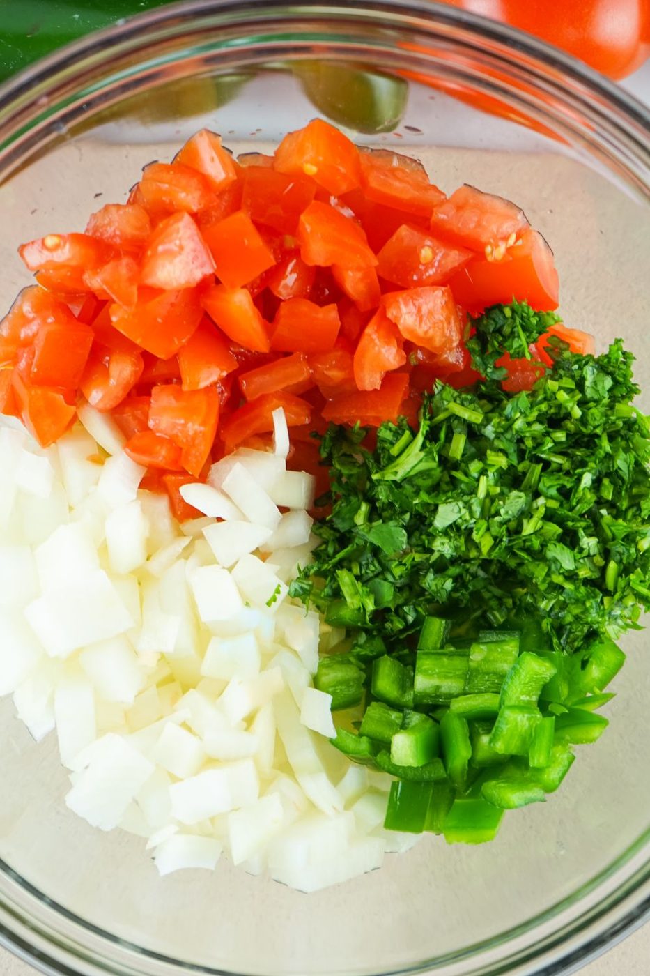 finely chopped tomatoes, onions, jalapeno and cilantro in a glass bowl on table