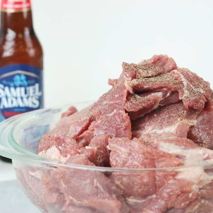 glass bowl of cut up pork with salt and pepper and beer in the background