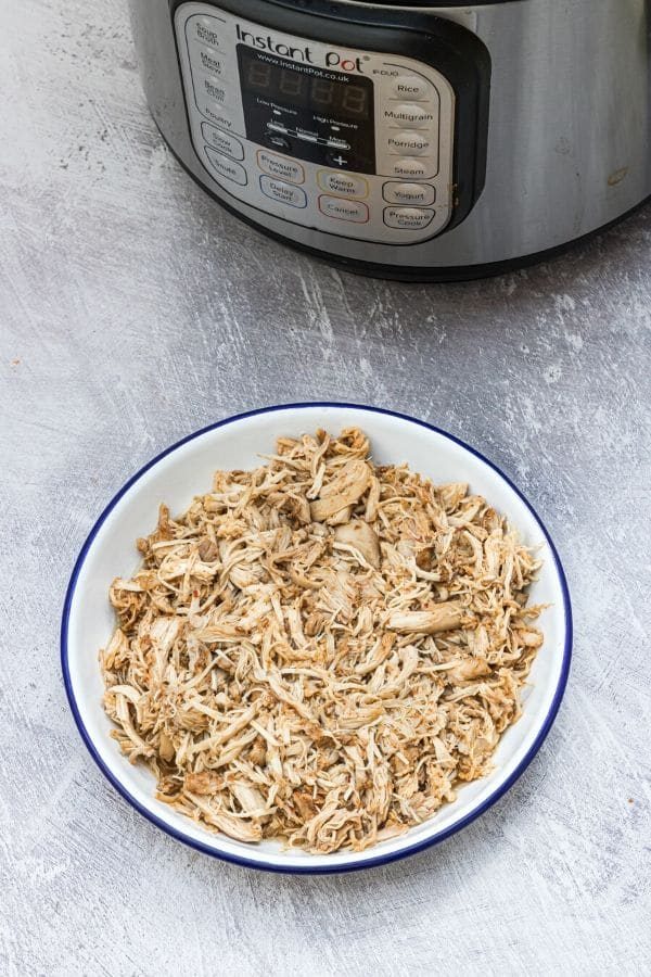 shredded chicken on a plate with Instant Pot behind it 