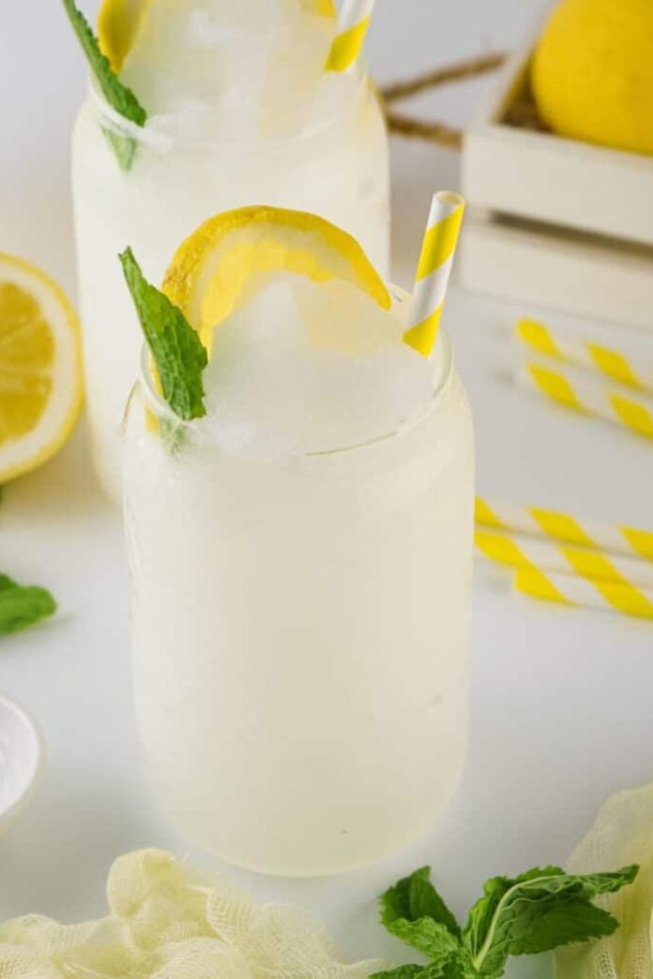 Lemonade Slushies in glasses on table with lemons, straws, and mint around table 