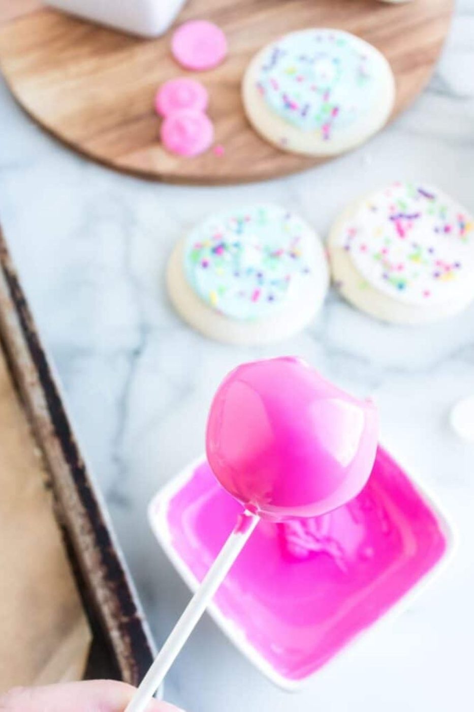 cookie truffle dipped in pink candy melts being held over the bowl 