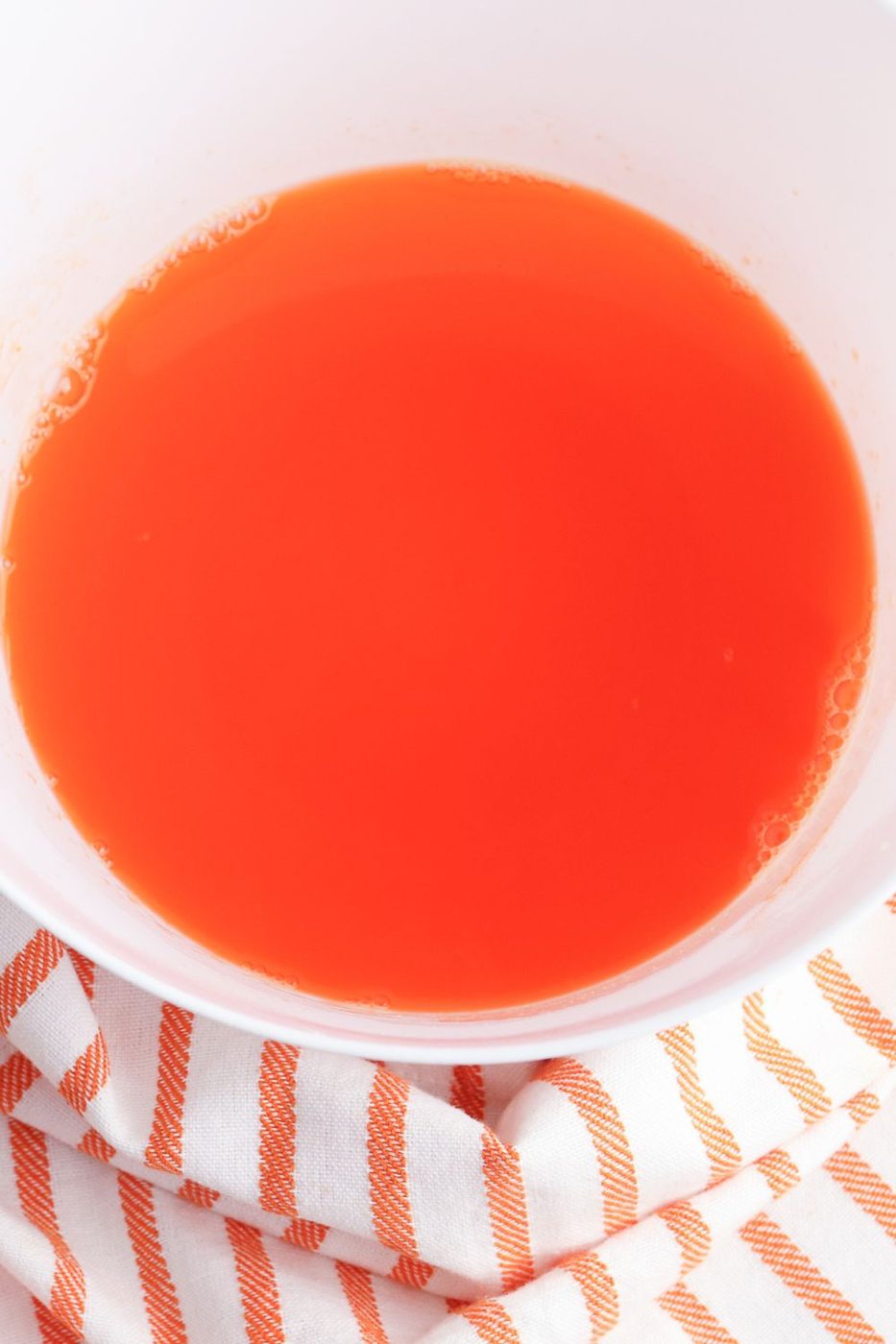 orange jello in a white bowl on table with a orange and white striped towel by it