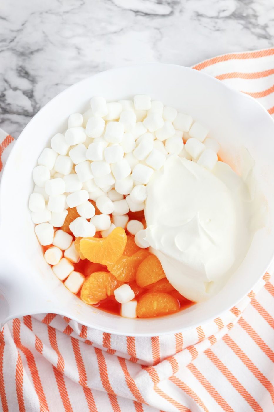 marshmallows, whipped cream, and oranges in a bowl with orange jello on table 