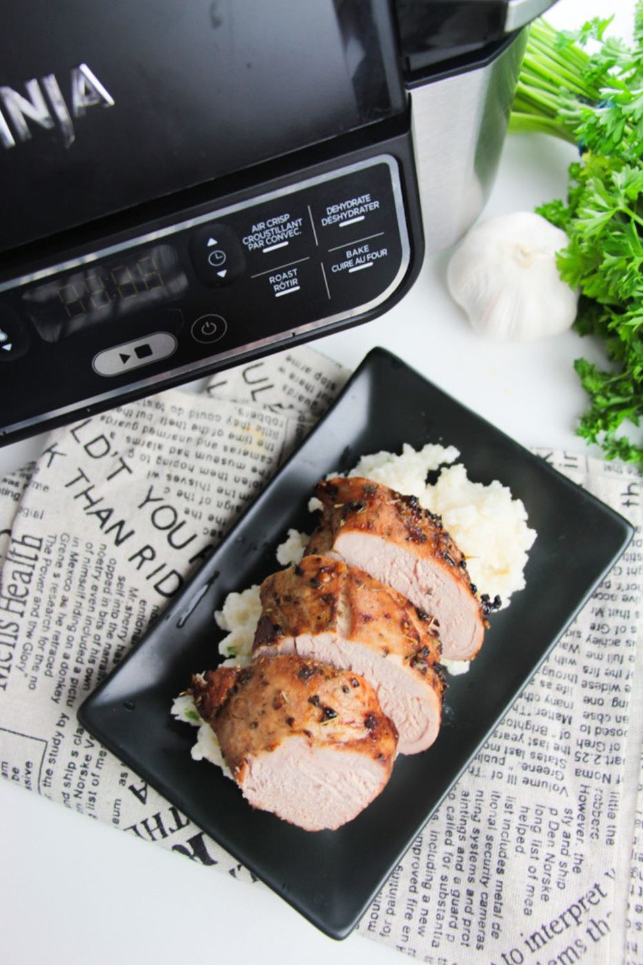 Air Fryer Pork Tenderloin sliced into medallions placed on a plate with mashed potatoes under it on a black plate with newspaper around the table 