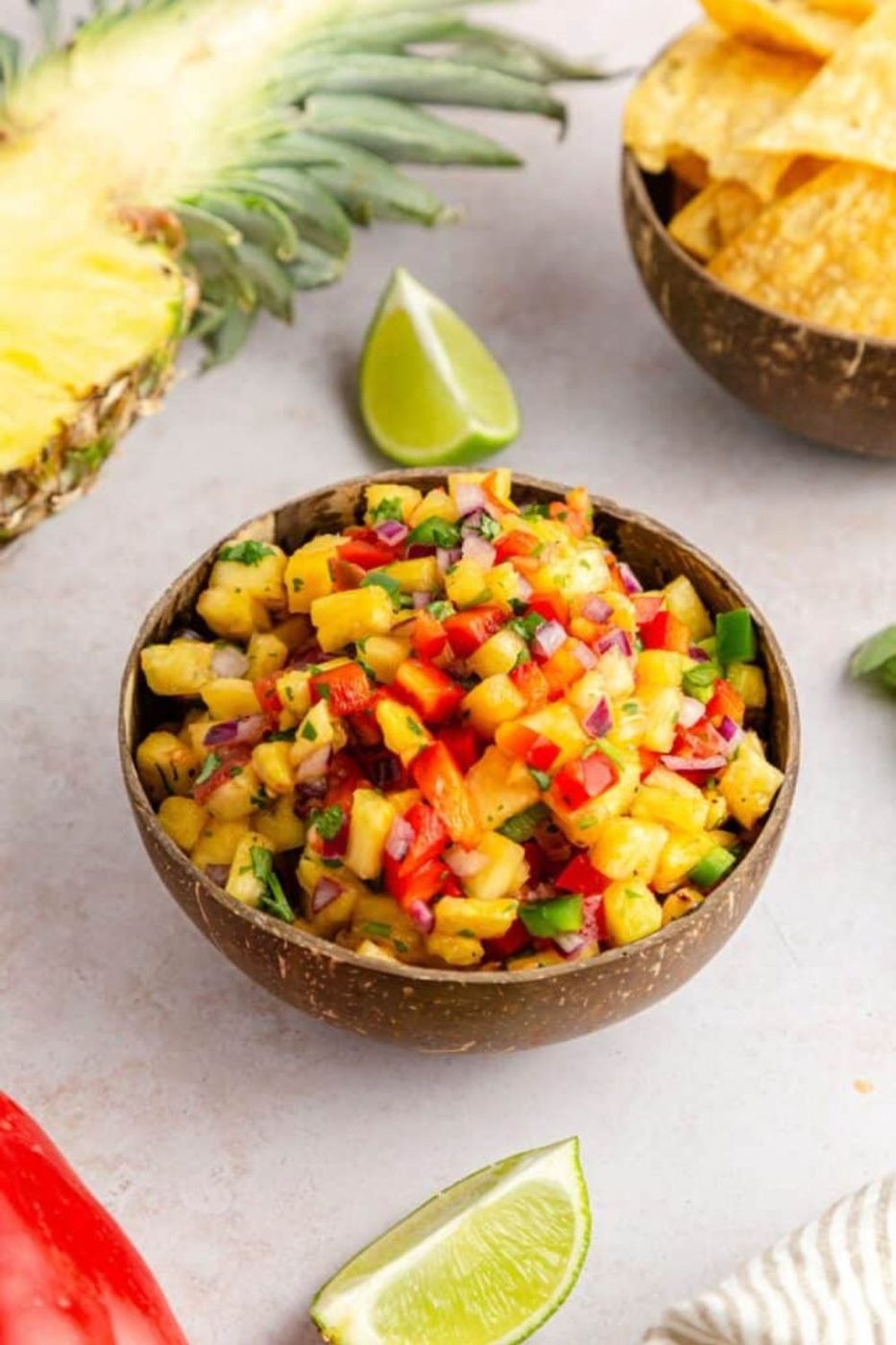 Pineapple Jalapeno Salsa in a bowl with chips to side and half a pineapple on table 