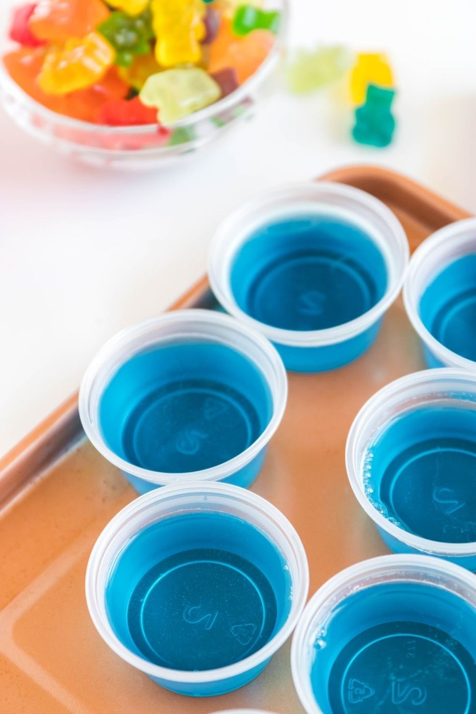 vodka jello shots on a tray with gummy bears in a bowl behind it