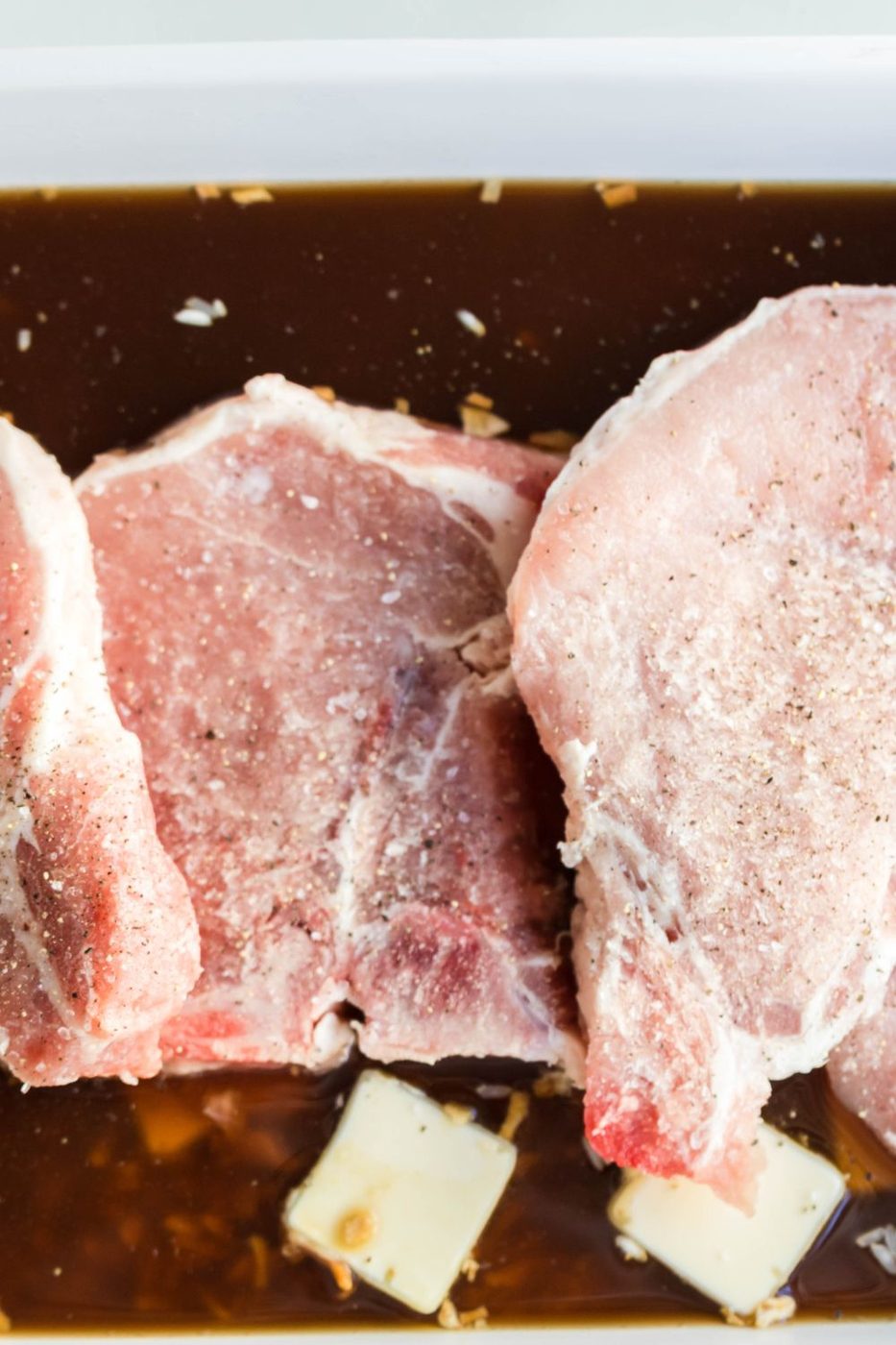 raw pork chops in a baking dish that is seasoned with salt and pepper 