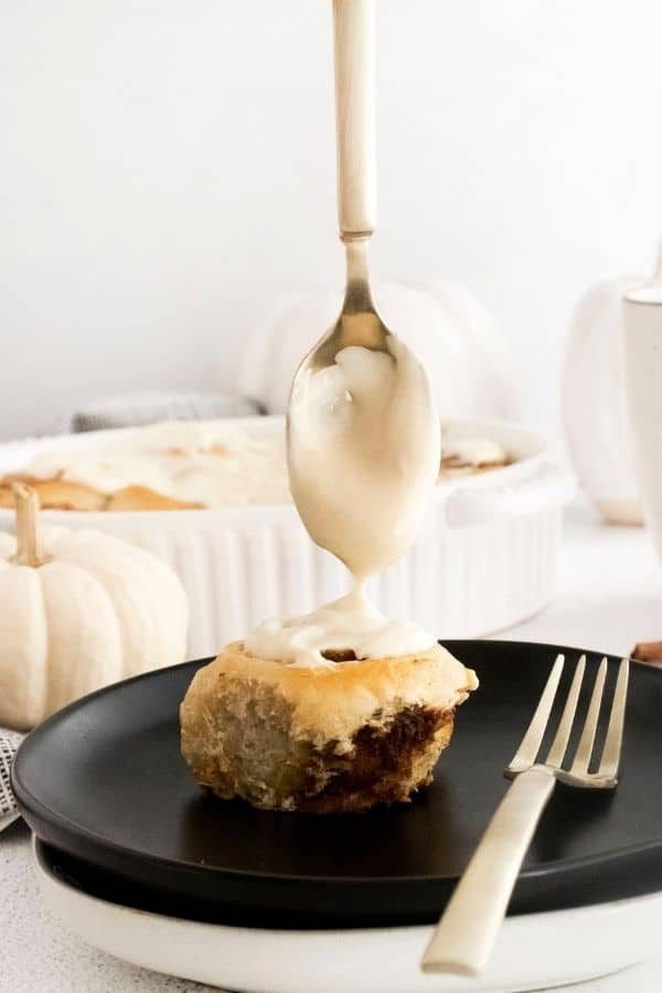 drizzling frosting on cinnamon roll with pumpkin