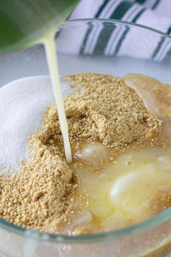 graham cracker crust being made with butter pouring into the bowl 