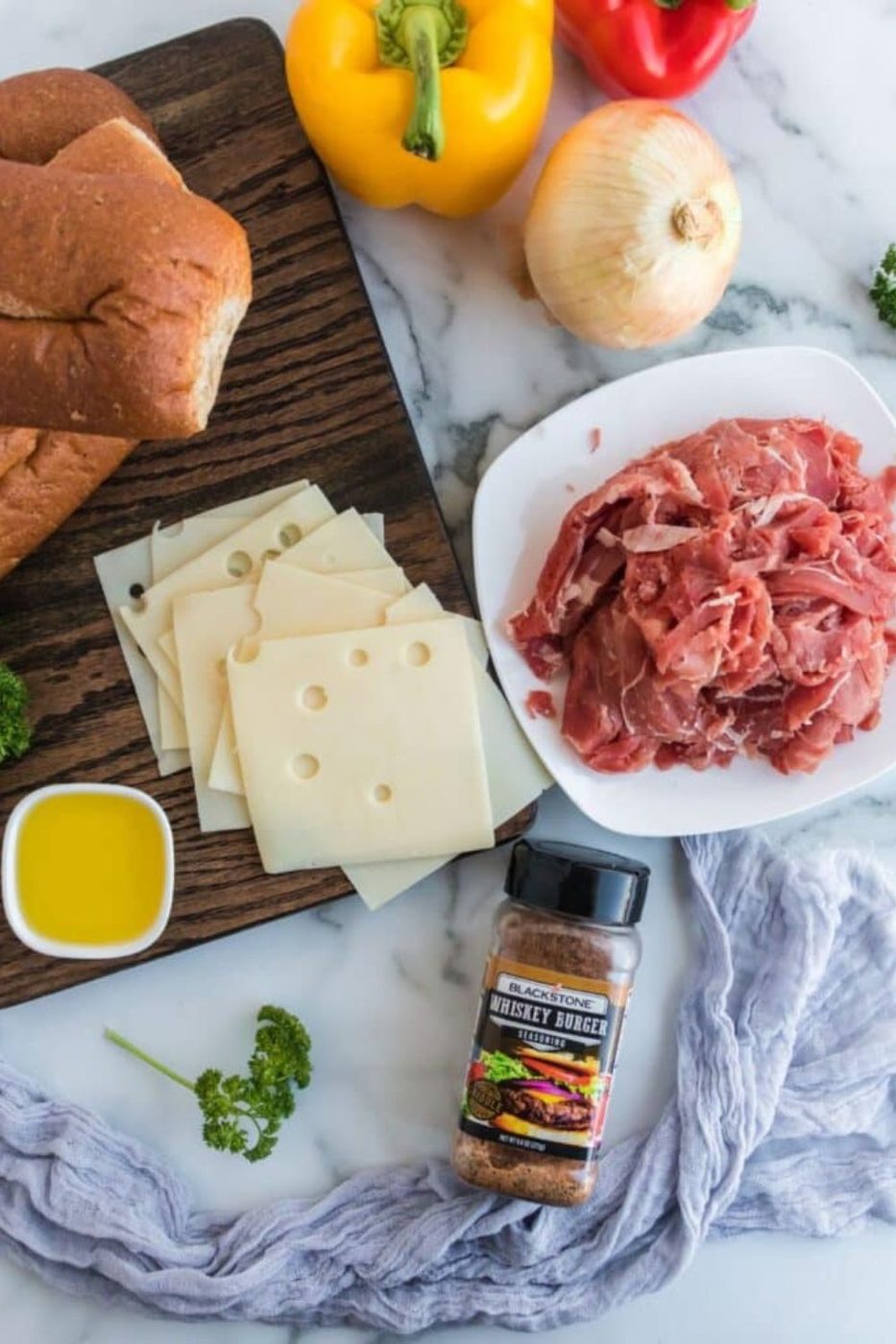 ingredients for shaved steak sandwiches on a marble countertop 