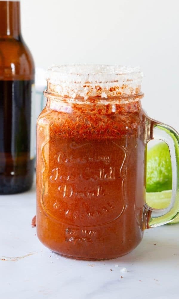 red beer on counter with beer bottle and limes in background 
