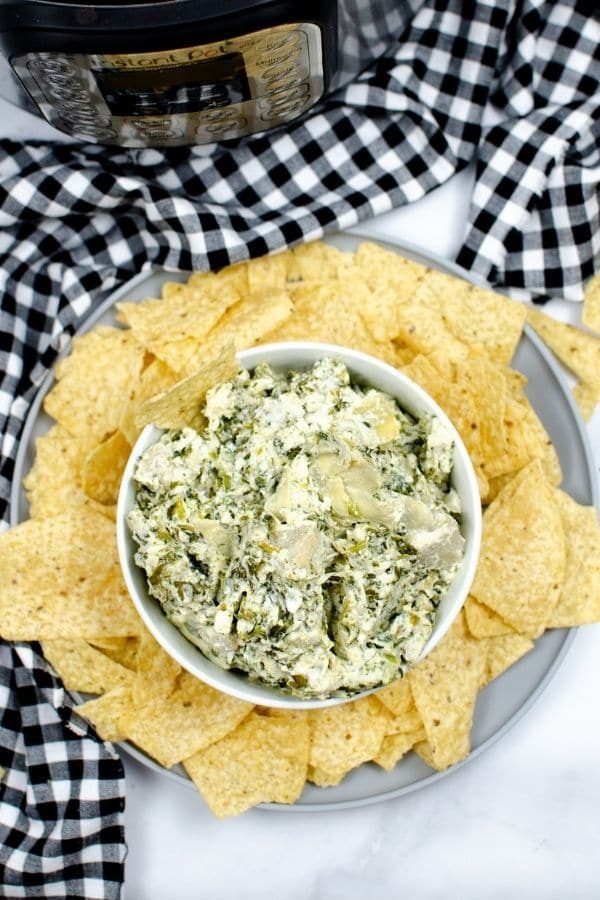 spinach dip on plate with chips around it by Instant Pot on table