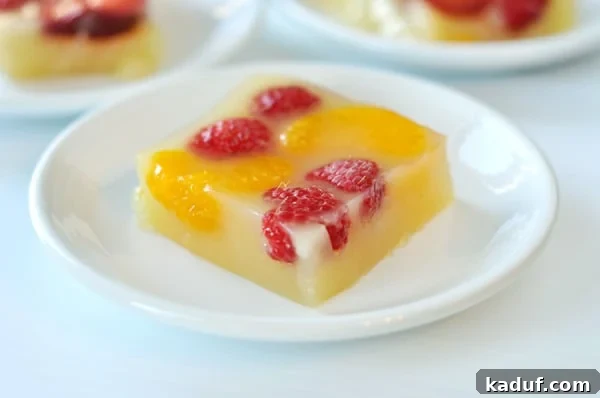 Sparkling Orange Gelatin from Scratch 2 A slice of homemade sparkling orange and berry gelatin, garnished with raspberries and mandarin orange segments, presented on a white plate.