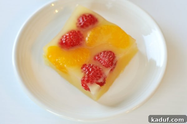 Sparkling Orange Gelatin from Scratch 3 An overhead view of a glistening slice of homemade sparkling orange and berry gelatin, showing whole raspberries and mandarin orange segments suspended within the vibrant orange setting.