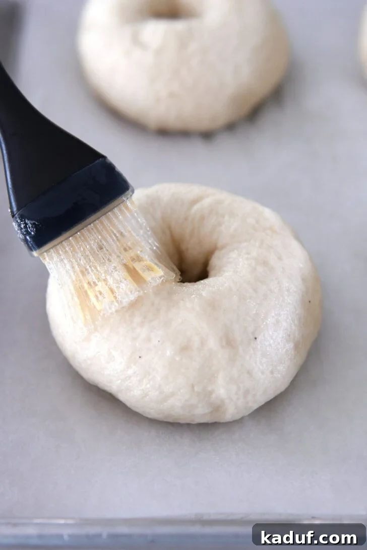 The Ultimate Homemade Bagel Recipe 10 Brushing egg wash on boiled bagel before baking.