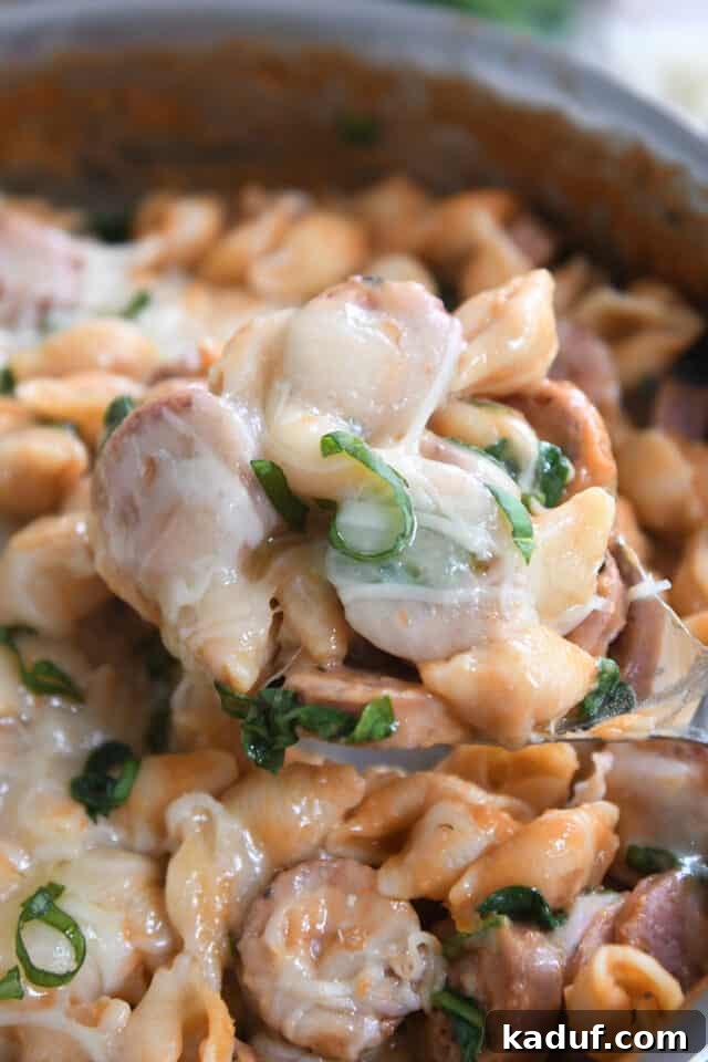 Tuscan Creamy Skillet Pasta 2 Spoon scooping up serving of pasta shells, fresh basil, sausage and cheese from a pan.