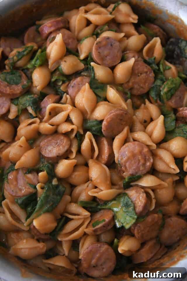 Tuscan Creamy Skillet Pasta 5 Cooked pasta shells with sausage, spinach, and sauce mixed in a deep pan.