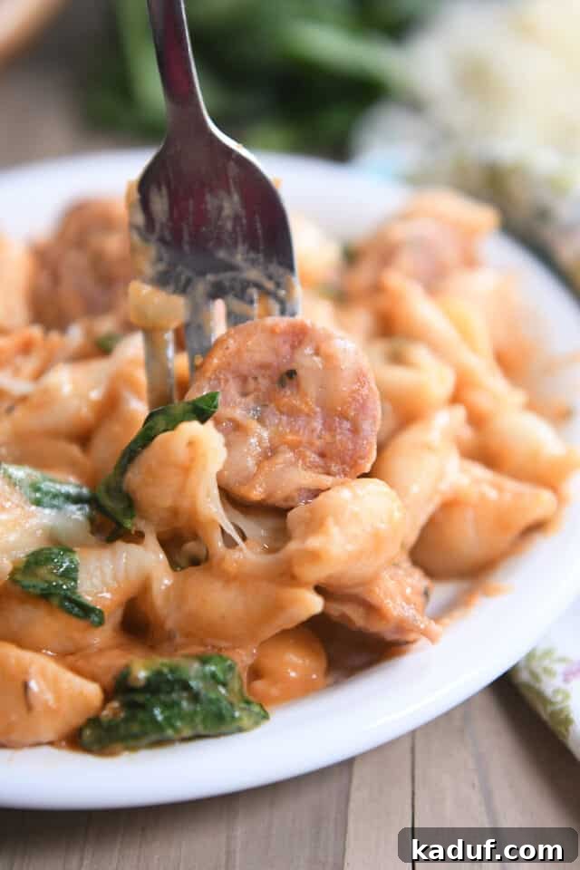 Tuscan Creamy Skillet Pasta 8 Fork scooping a perfect bite of creamy pasta shells and sausage on a white plate, garnished with fresh basil.