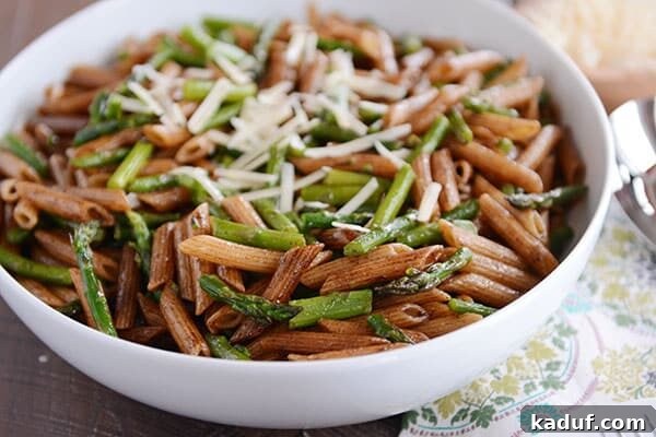 A large white bowl filled with penne pasta coated in balsamic sauce, adorned with asparagus pieces and shredded Parmesan on top.