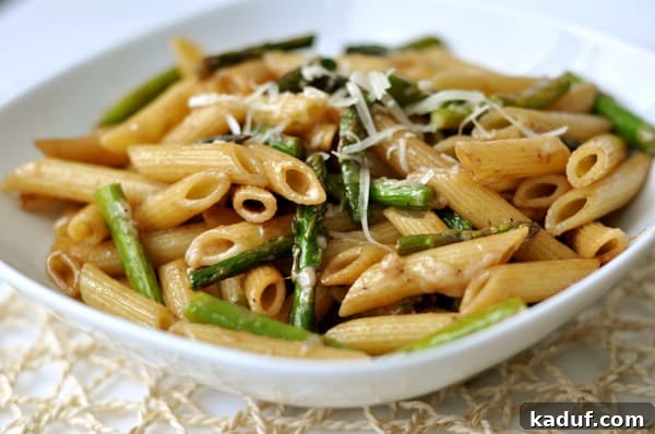A pristine white bowl showcasing perfectly cooked penne pasta and vibrant green asparagus pieces, a testament to simple elegance.