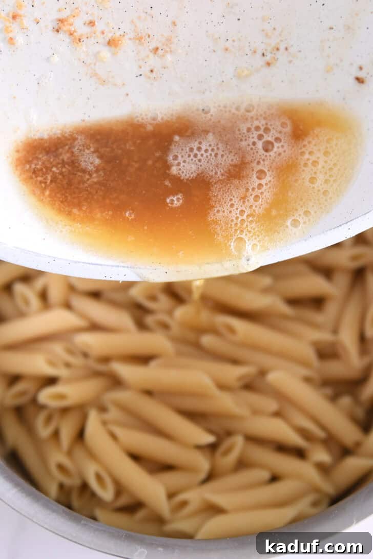 Golden brown butter being poured over freshly cooked penne pasta, adding depth of flavor.