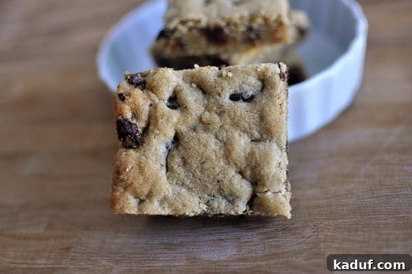 Golden Oat Chocolate Chip Squares 11 A single delectable oatmeal chocolate chip cookie bar resting next to a white bowl, showcasing its chewy texture and abundant chocolate chips.